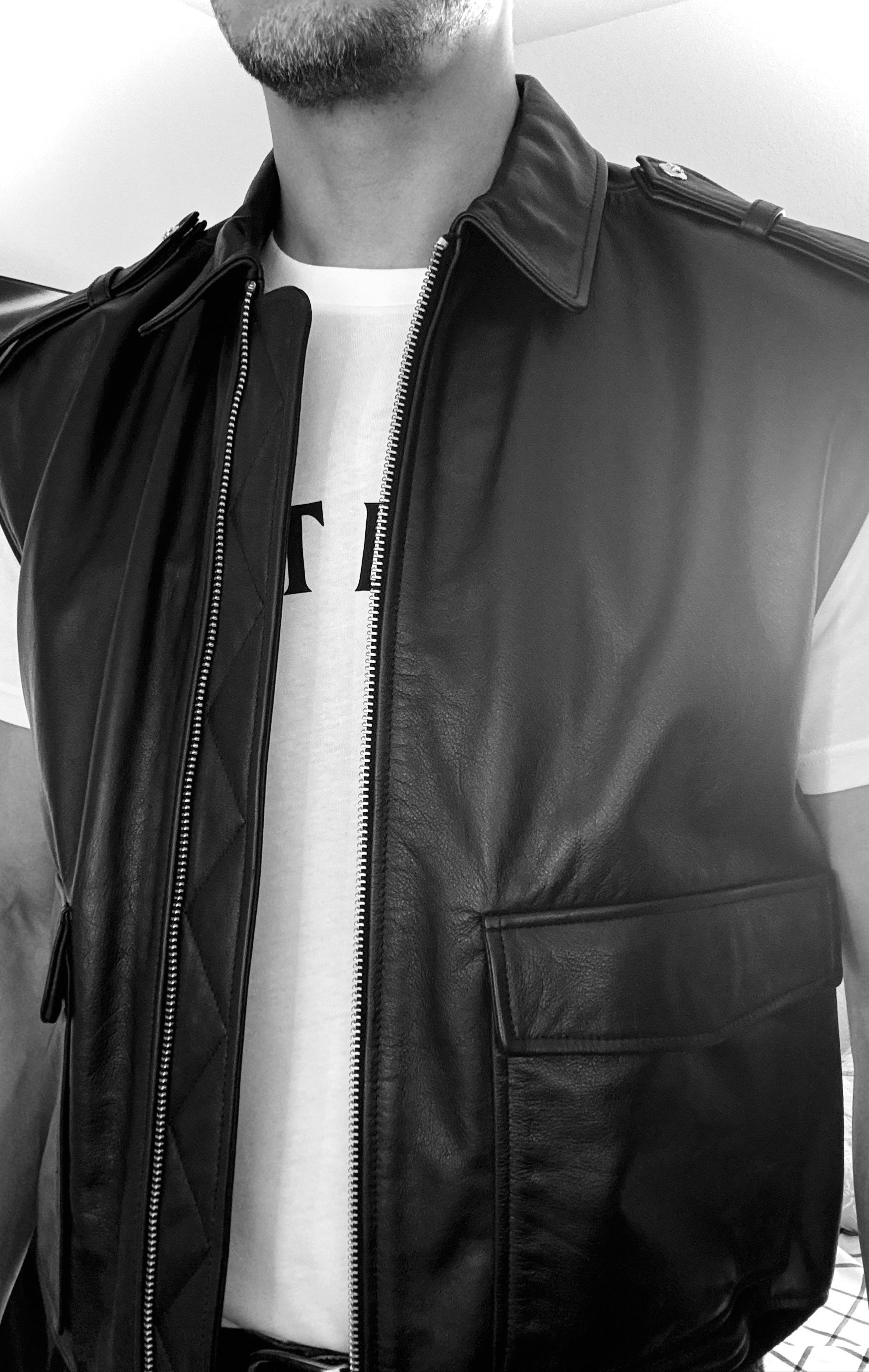 Person wearing a black leather vest over a white shirt with a logo.